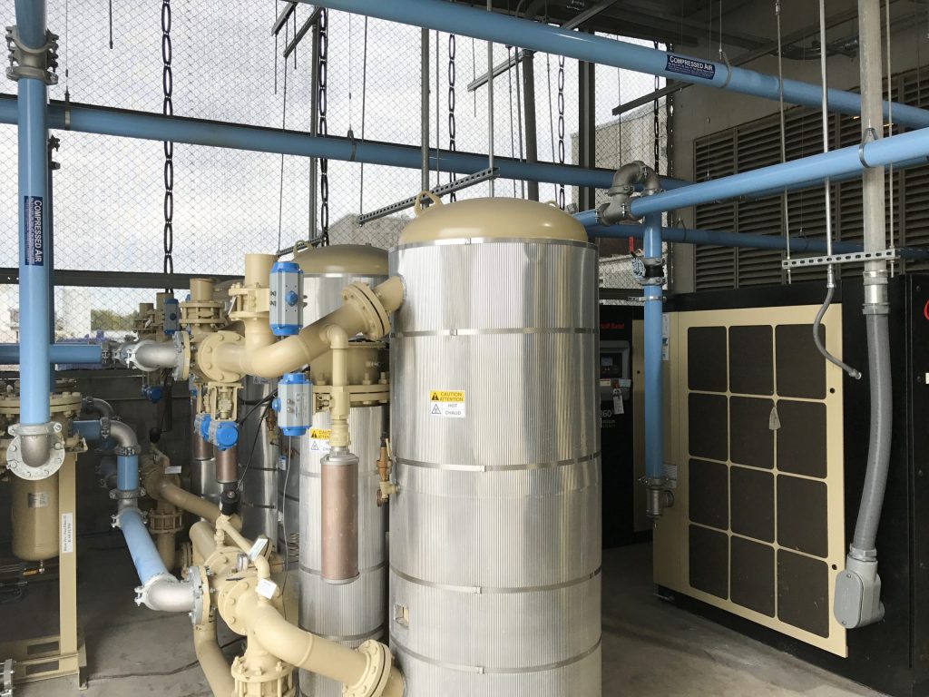 Industrial filtration system with pipes, valves, and a large cylindrical tank, installed in a facility with exposed infrastructure and incorporating Arle Compressors of Florida.