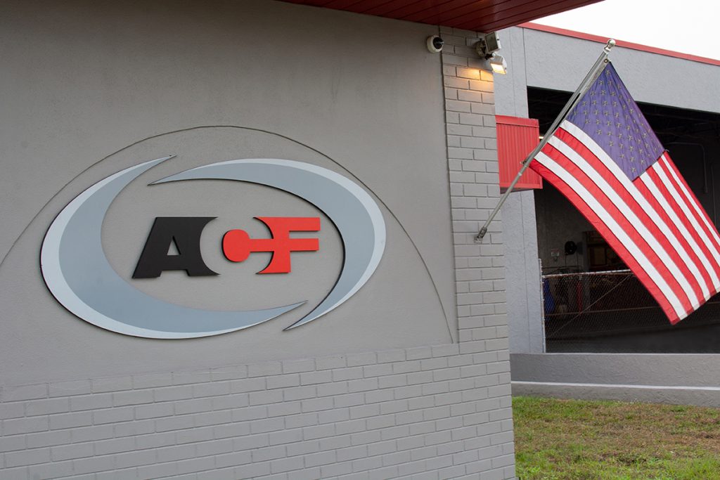 Logo of "Arle Compressors of Florida" emblazoned on a building's exterior wall with an American flag hanging beside it.