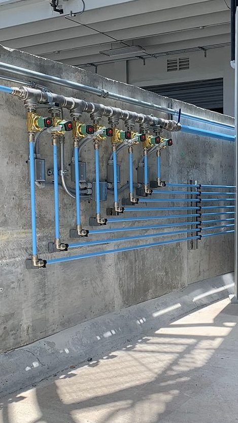 Neatly organized Arle Compressors of Florida industrial piping system mounted on a concrete wall, featuring valves and gauges with blue conduit pipes running vertically alongside.