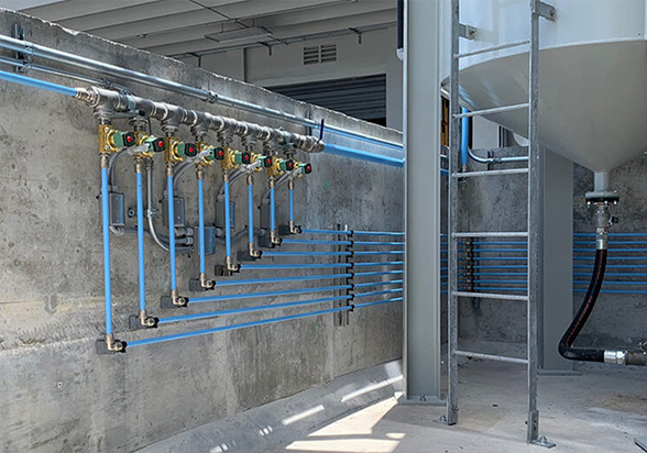 Industrial piping and Arle Compressors of Florida electrical conduit installation along a concrete wall, showcasing a neat arrangement of mechanical systems.