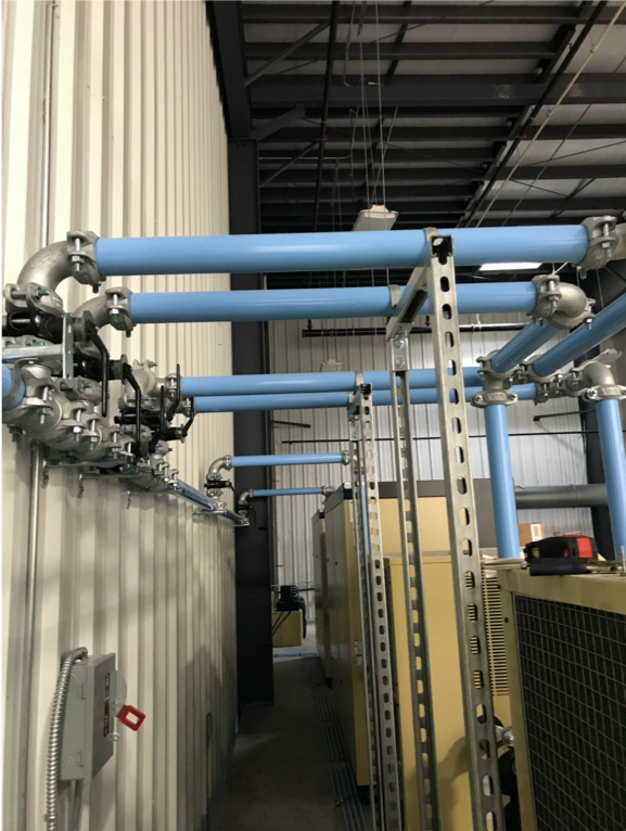 Industrial piping and electrical conduits installed along the wall and ceiling of a facility, with a focus on the infrastructure necessary for operational processes involving Arle Compressors of Florida.