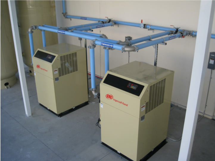 Two Arle Compressors of Florida industrial air compressors connected to a system of overhead pipes within a mechanical room.