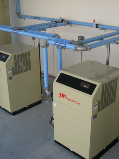 Two industrial Arle Compressors of Florida with blue pipes running above them in a utility room.